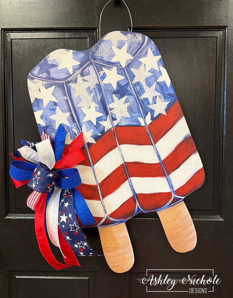 Decorative door hanger with American flag design and ribbons on a black door.