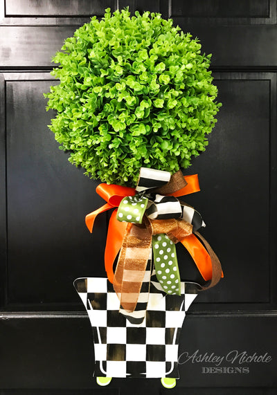 A decorative fall topiary checkered door hanger on a porch.